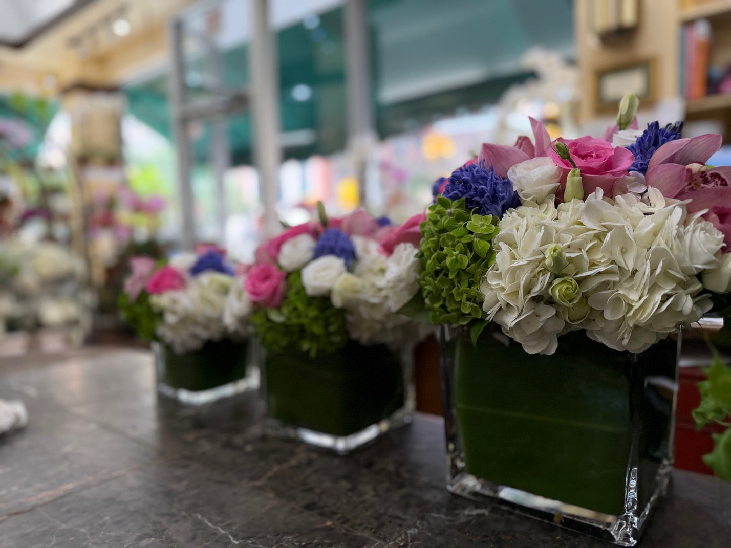 
                    
                      Three Eliana leaf-lined glass cubes on the Jerome Florists counter, front one in focus, storefront windows blurred behind
                    
                  