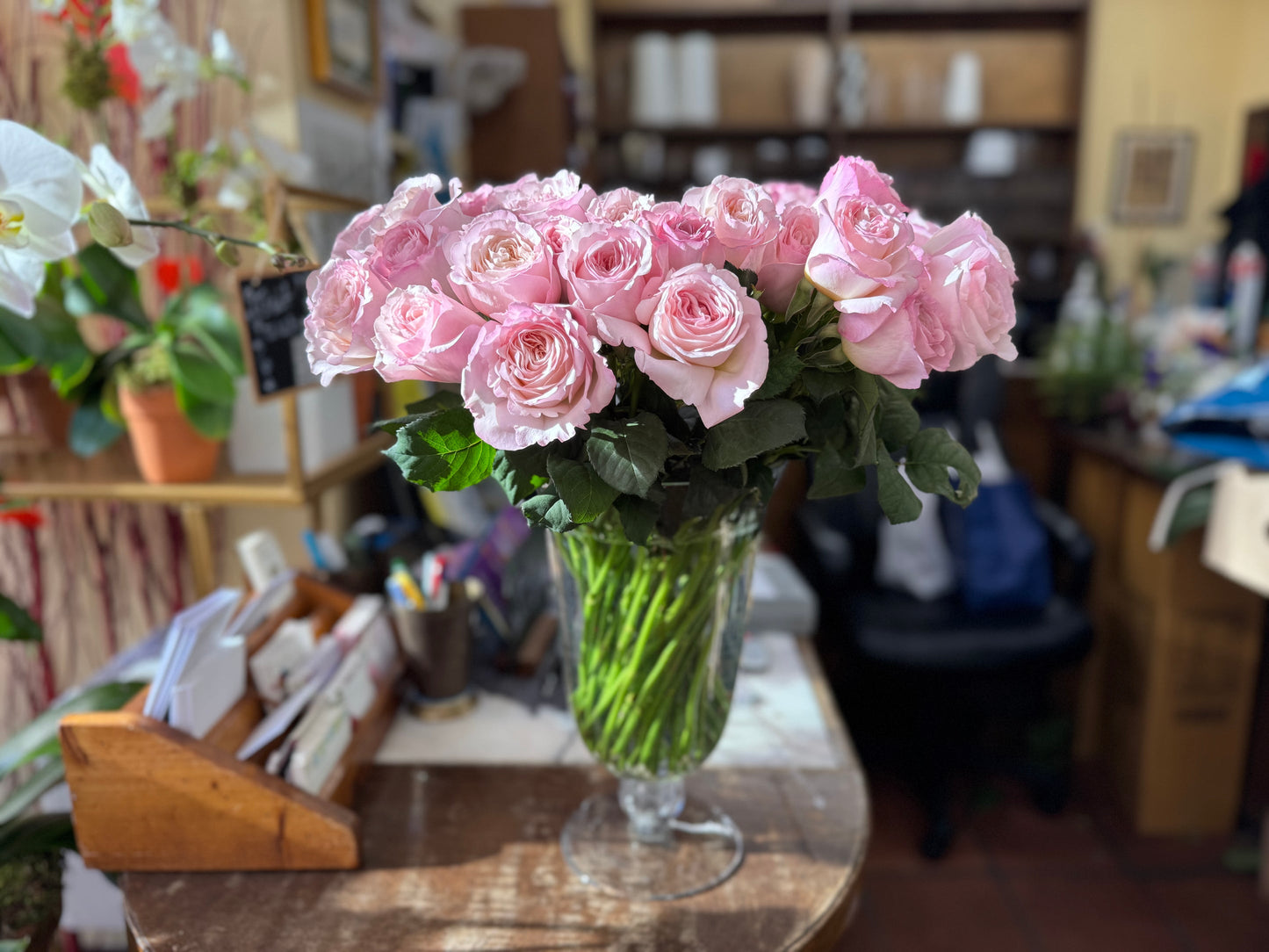 Bouquet of pink garden roses in a glass vase on the wooden counter of Jerome Florists