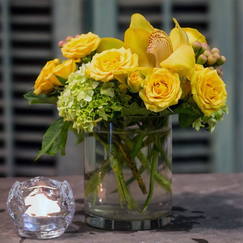 Beautiful yellow roses anchor this arrangement that also includes cymbidium orchid heads and green hydrangea - Jerome Florists NYC